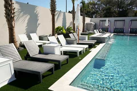 Resort pool area with white lounge chairs, palm trees, umbrellas, and manicured lawn