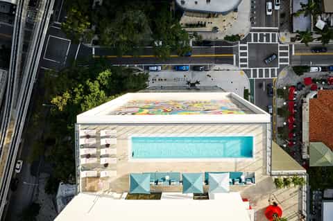 Overhead view of rooftop pool with colorful floor art, lounge areas, and urban street surroundings