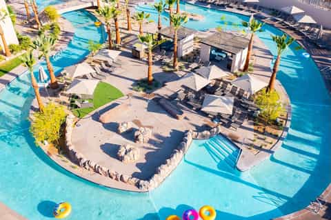 Aerial view of resort pool complex with palm trees, loungers, and sandy beach areas