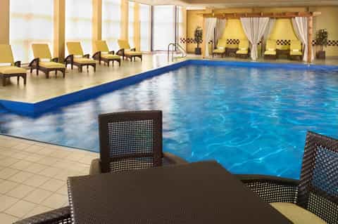 Indoor swimming pool with yellow lounge chairs, draped cabanas, and large windows