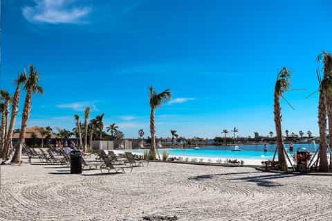Beach resort with turquoise lagoon, white sand, lounge chairs, palm trees, and beachfront buildings