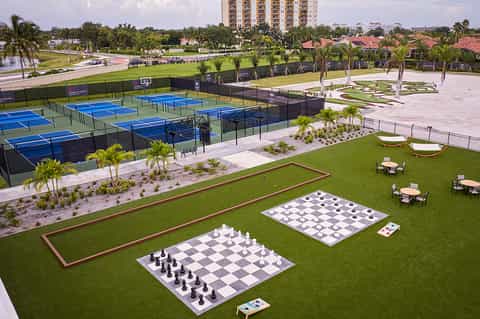 Resort recreational facilities with tennis courts, lawn games, palm trees, and residential building