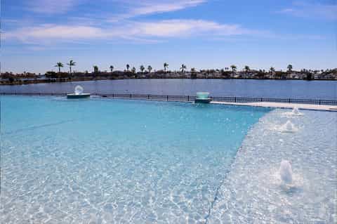 Crystal-clear lagoon-style pool with sandy beach entry and palm-lined waterfront in background