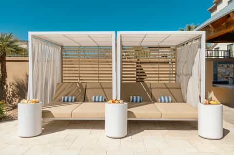 Two white cabanas with retractable roofs and striped cushions on sunny beachfront patio