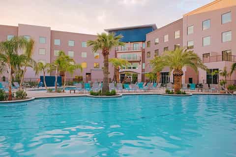 Resort pool surrounded by pink hotel buildings, palm trees, and turquoise lounge chairs