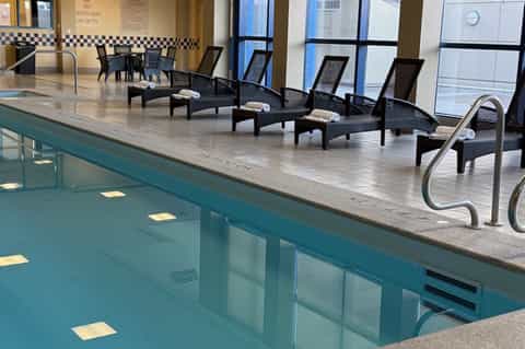 Indoor pool deck with black lounge chairs, large windows, and modern facilities by the water
