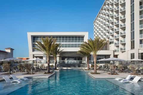 Resort outdoor pool with palm trees, loungers, and multi-story hotel building in clear daylight