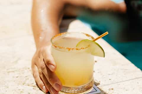 Hand holding margarita with lime and salted rim by pool with turquoise water in background