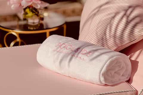 Rolled white spa towel with embroidered text on pink seating area