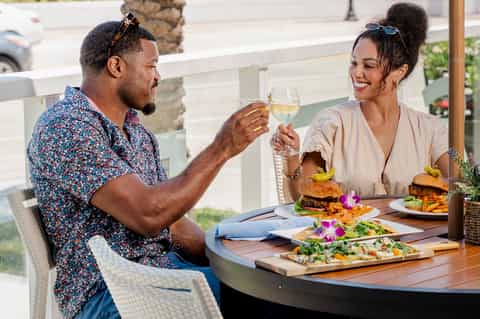 Couple toasting with white wine at outdoor dining table with burgers and salads