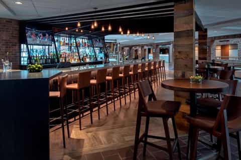 Modern hotel bar with dark wood counter, copper pendant lights, brick walls, and wooden flooring