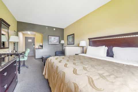 Hotel bedroom with queen bed, work desk, yellow and gray walls, and bathroom entrance