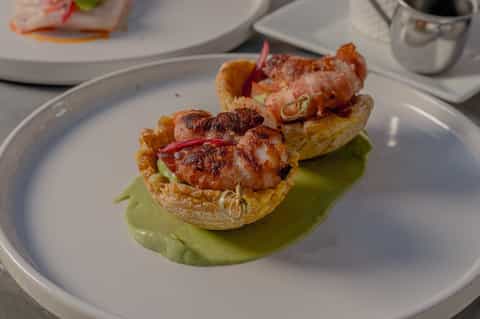 Plated appetizer featuring seared shrimp on crispy base with green sauce and garnish