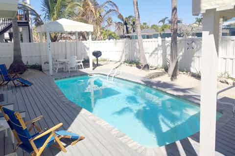 Beach cottage private pool with wooden deck, palm trees, white fence, and lounge chairs
