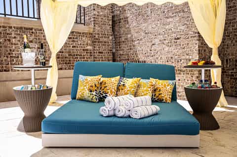 Spa relaxation lounge with blue daybed, yellow curtains, decorative pillows, and rolled towels
