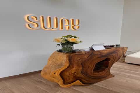 Modern hotel lobby entrance with illuminated 'sway' signage and natural wood reception desk