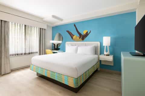 Colorful modern hotel bedroom with turquoise accent wall, white bedding, and playful wall art