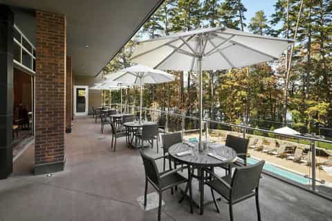 Elevated patio with white umbrellas, dining tables, and pool views through trees