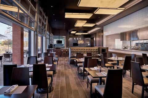 Modern hotel restaurant with dark wood tables, brick accents, and floor-to-ceiling windows