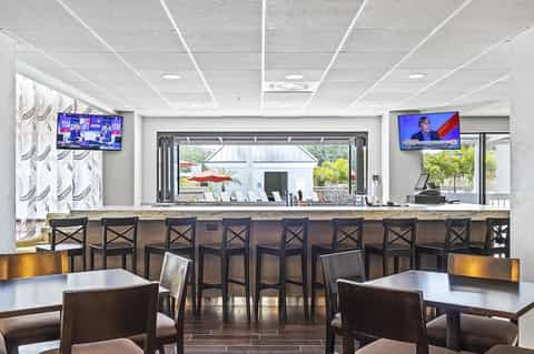 Hotel bar and lounge area with seating, counter, TV screens, and views to outdoor patio space