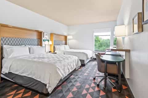 Modern hotel bedroom with two queen beds, geometric patterned headboards, and work desk