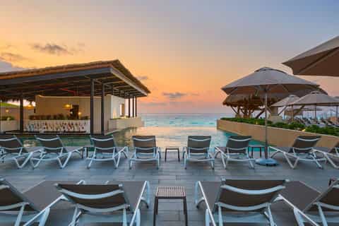 Beachfront bar and lounge at sunset with umbrellas, chairs, and ocean views