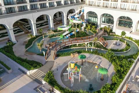 Aerial view of resort courtyard with lazy river, water playground, and white arched architecture