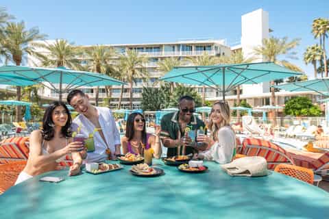Beachfront resort guests enjoying cocktails under turquoise umbrellas with palm trees