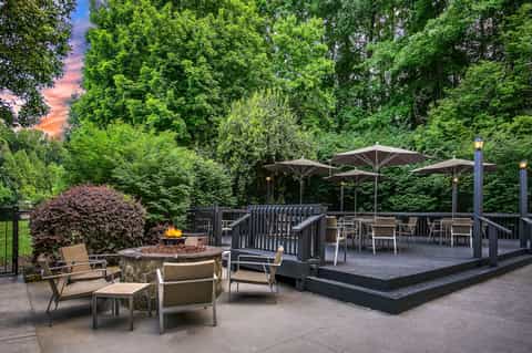 Outdoor terrace with fire pit, umbrellas, deck seating, and forest backdrop at dusk