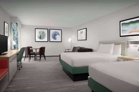 Hotel room with two queen beds, green accents, botanical artwork, and modern furnishings