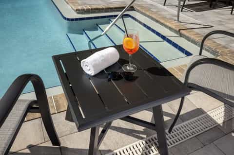 Poolside table with towel, sunglasses, and cocktail overlooking turquoise swimming pool