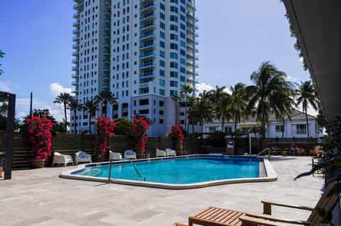 Waterfront hotel pool with tropical landscaping, high-rise building, and palm trees