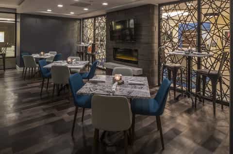 Contemporary dining room with blue chairs, patterned tables, fireplace, geometric window screens