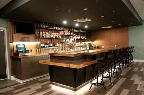 Contemporary bar with wood top, shelving display of liquor bottles, and black bar stools