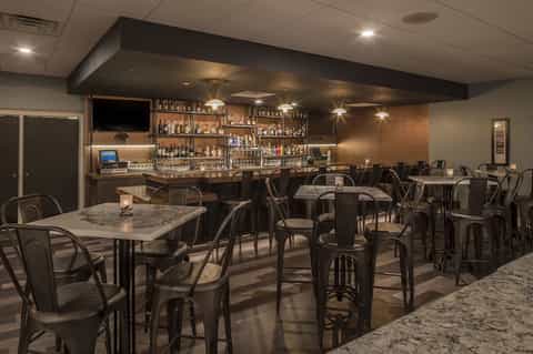 Modern lounge bar with dark furnishings, high-top tables, full bar counter, and contemporary lighting