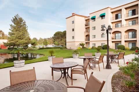 Hotel exterior with patio seating overlooking pond and manicured green lawn