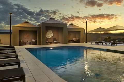 Modern resort pool with architectural pavilions, lounge chairs, and sunset lighting