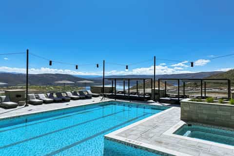 Modern infinity pool with mountain views, lounge chairs, and spa hot tub at sunset
