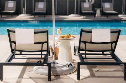 Two lounge chairs by resort pool with umbrella, food, and beverage service setup