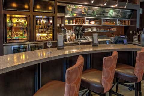 Upscale bar interior with illuminated liquor cabinets, dark wood, and bar seating