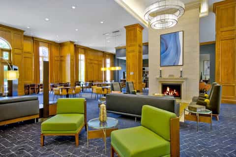 Elegant lobby with fireplace, golden wood columns, lime-green accent chairs, and modern chandelier lighting