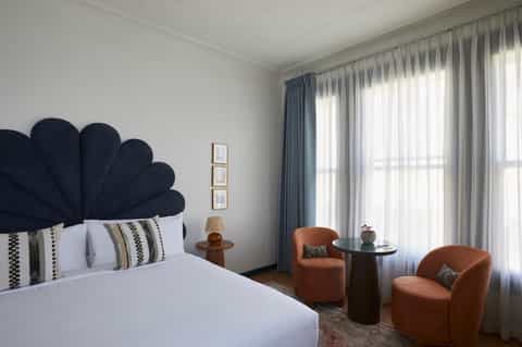 Hotel bedroom with navy shell-shaped headboard, terracotta chairs, and layered curtains