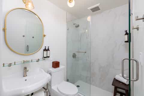 Modern bathroom with marble shower, gold-framed circular mirror, and white fixtures