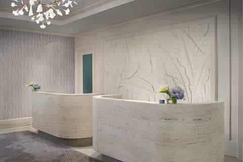 Elegant curved reception desk in white marble with textured wall art and flower arrangements