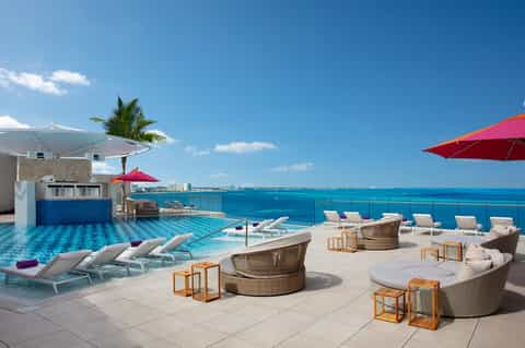 Luxury beachfront pool deck with loungers, ocean views, and pink umbrellas