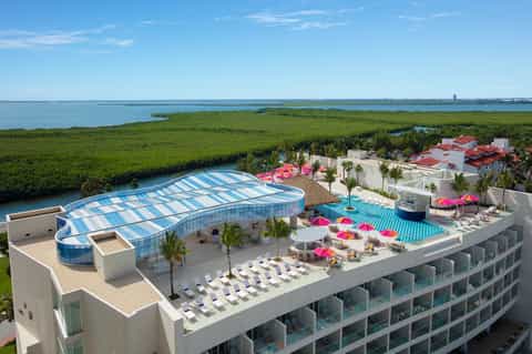 Aerial view of beachfront resort with blue striped pool cover, pink umbrellas, and bayside marsh landscape.