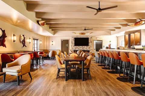 Spacious lounge with wooden ceiling beams, orange and white seating, bar, and fireplace