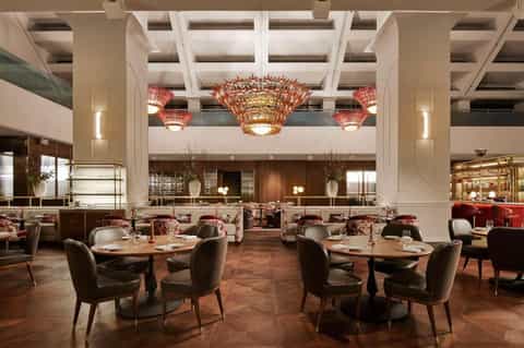 Contemporary restaurant dining area with high ceilings, red chandeliers, round tables, and modern design