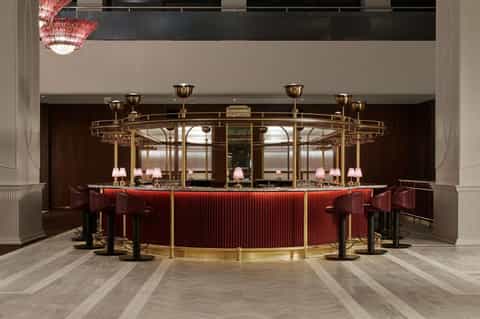 Elegant curved bar with red ribbed panels, brass fixtures, and pink chandeliers in Art Deco style