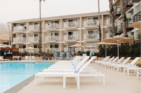 Three-story beachfront hotel with cream-colored balconies, palm trees, and white lounge chairs by pool